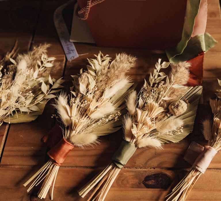 Dried floral buttonholes tied with pastel coloured ribbons set on wooden table