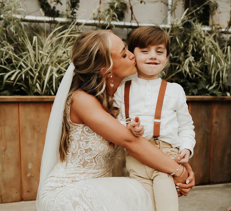 Bride kisses child wearing braces and chinos on the cheek at wedding 