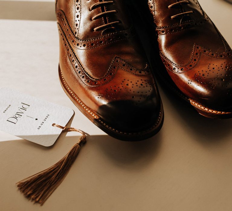 Brown brogues next to white table place name with monochrome typography and brown tassel 