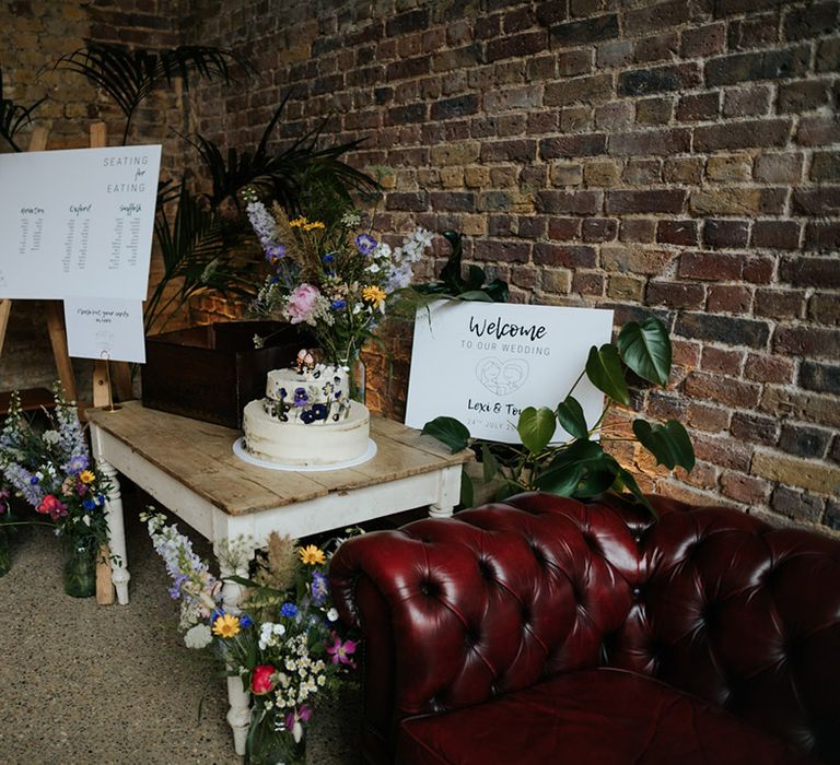 Welcome wedding sign with seating chart and colourful wildflower wedding bouquets with semi-naked two-tier wedding cake 