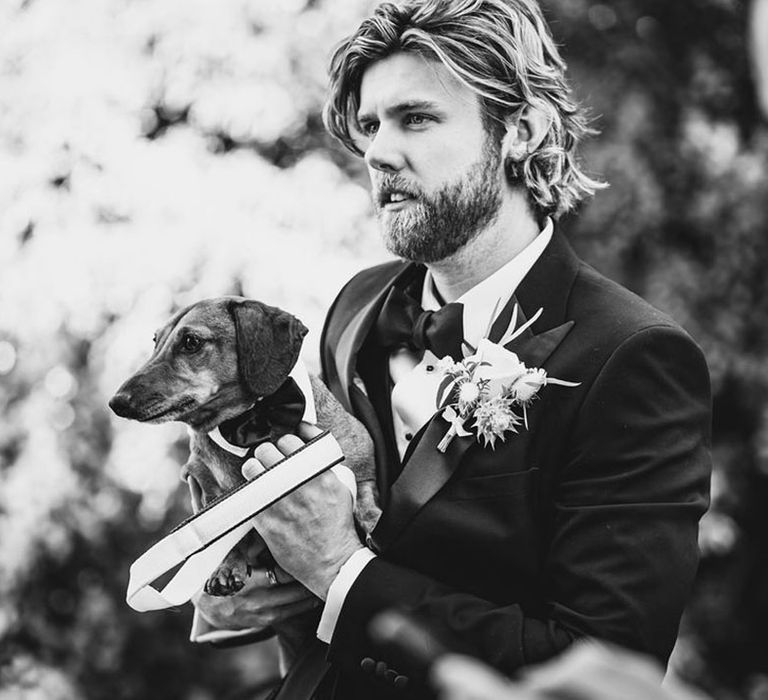 Groom in black tuxedo with dachshund puppy also in a tuxedo dog wedding outfit 