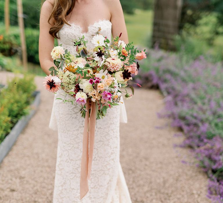 Bride in strapless lace puddle train wedding dress holding wildflower wedding bouquet with red, pink, peach and white flowers