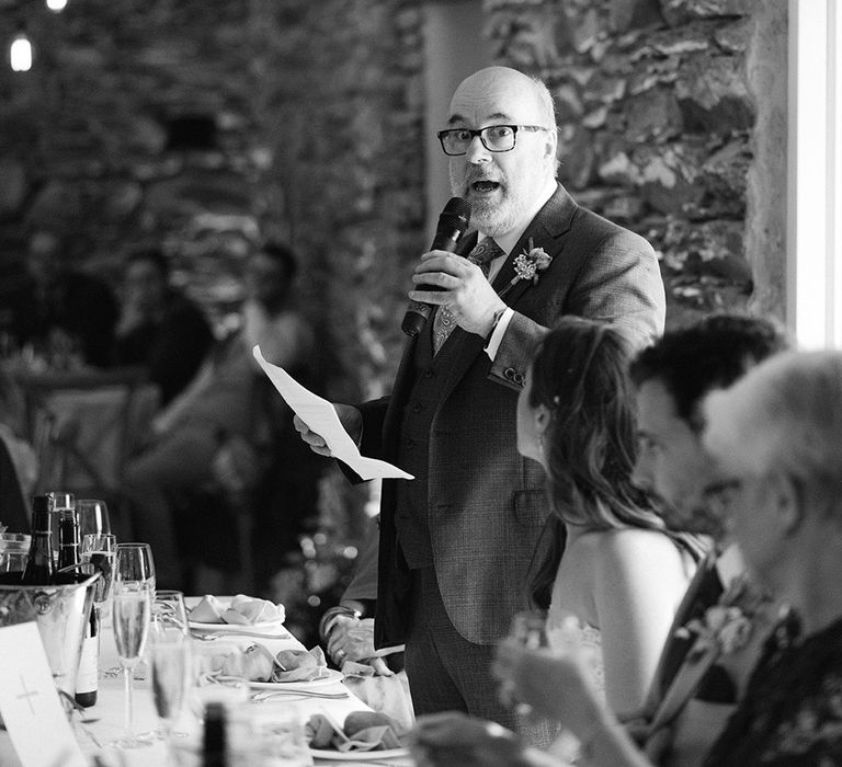 Father of the bride gives his speech at the wedding wearing paisley tie with hanging naked lightbulb decoration 