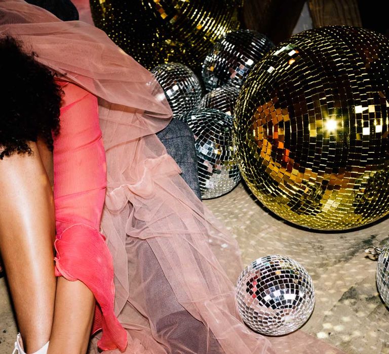 Bride in a red wedding dress with pink veil and white boots sitting next to silver and gold disco balls at The Canary Shed wedding venue