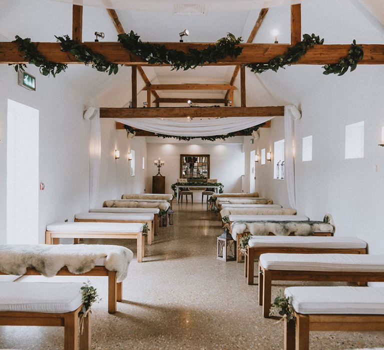 Southend Barns wedding with wooden benches with white covering and decorative greenery on exposed beams