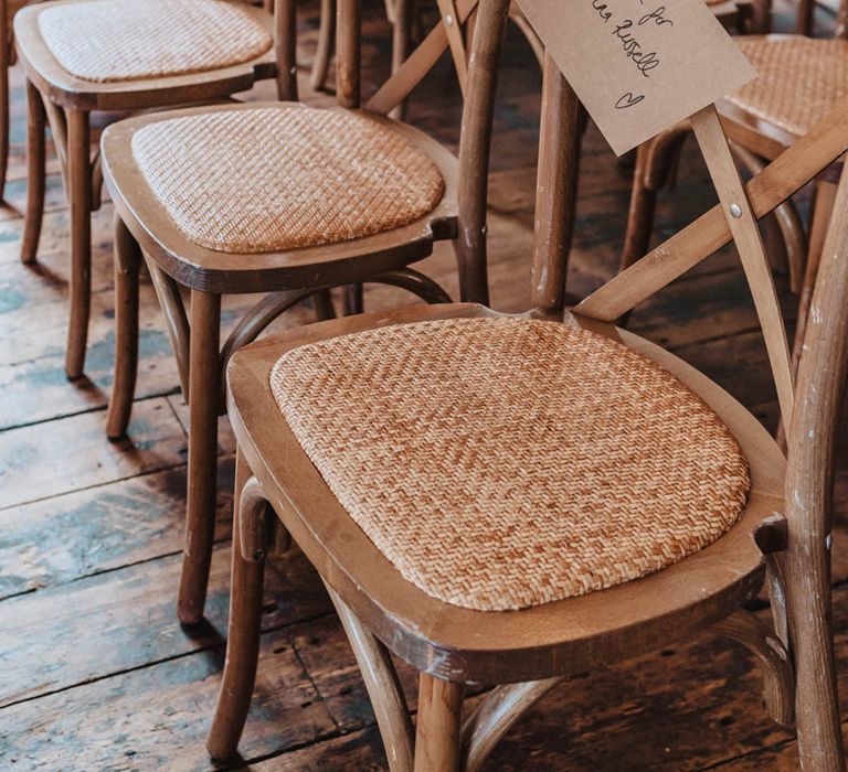 Light wooden rattan chairs for guests with brown name tags attached with blue ribbon