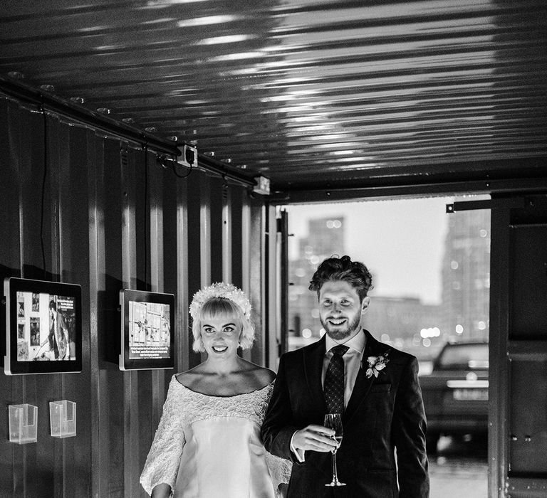 Bride in short wedding dress holding a bouquet walks into reception with groom holding glass of champagne