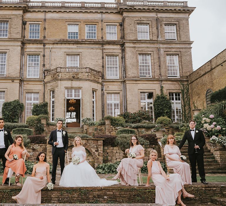 Wedding party shot of groom, groomsmen, bridesmaids and bride in front of country house venue 