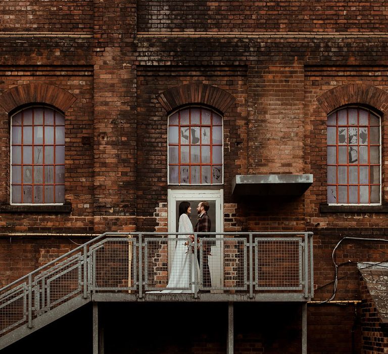 Bride & groom stand on staircase outside industrial setting on their wedding day