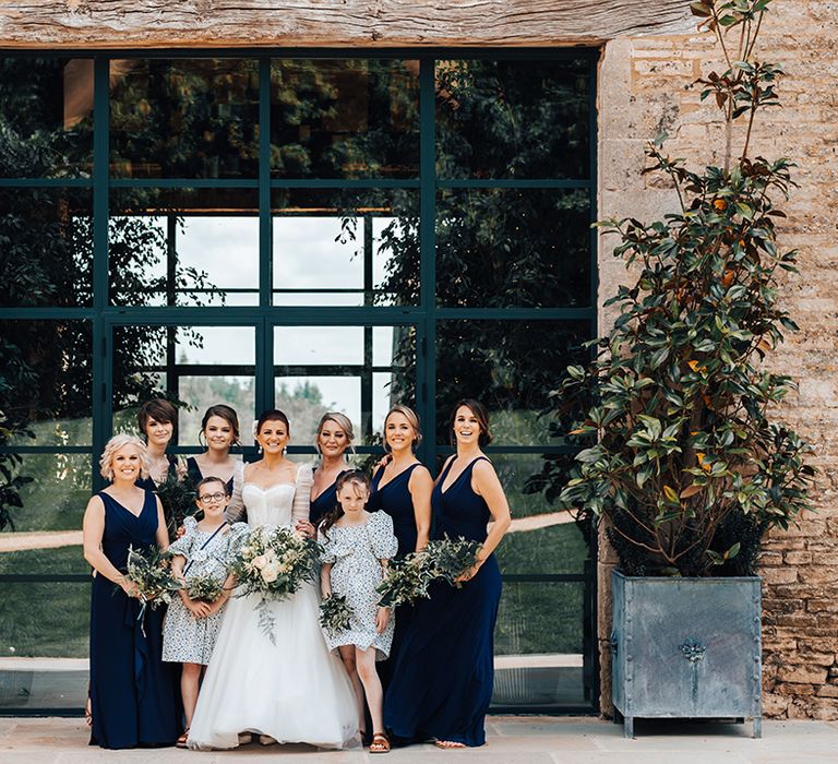 Bride in princess wedding dress with bridesmaids in navy blue dresses and younger bridesmaids in white dresses with blue flowers 