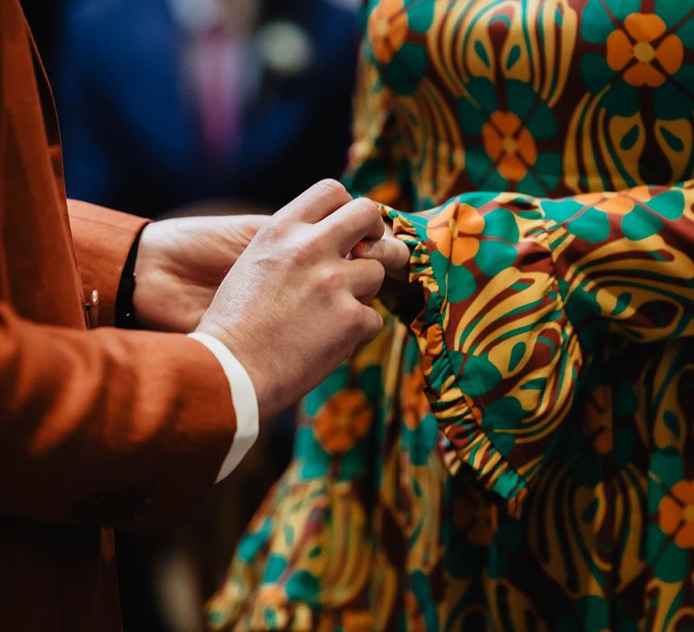 Groom places ring on his brides finger who wears brightly coloured wedding gown 