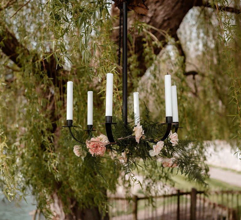 black hanging chandelier from a tree with white taper candles, pink roses and foliage decor 