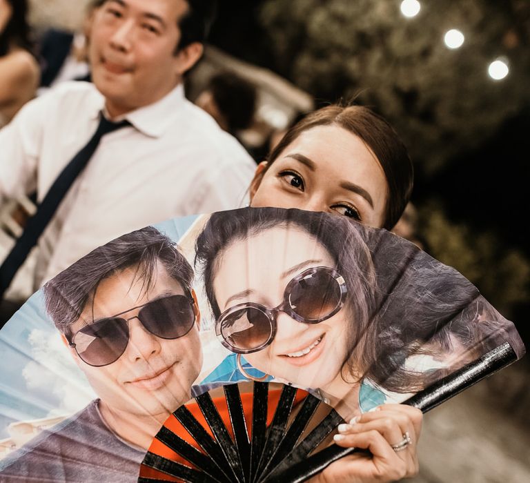 Wedding guest holds personalised fan with face of bride & groom inspired by drag brunches 