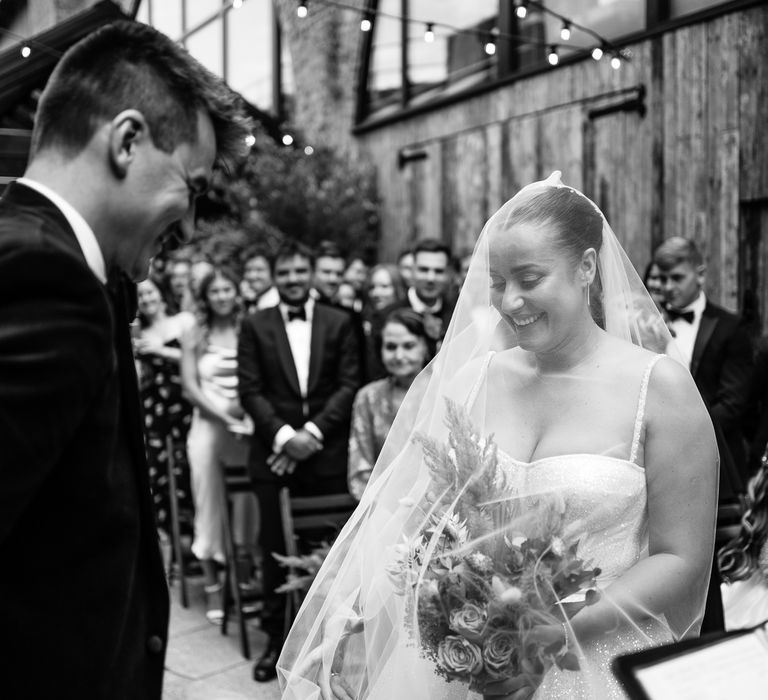 Bride wears floor-length veil across her face as she stands in front of her groom during outdoor wedding ceremony at the 100 Barrington