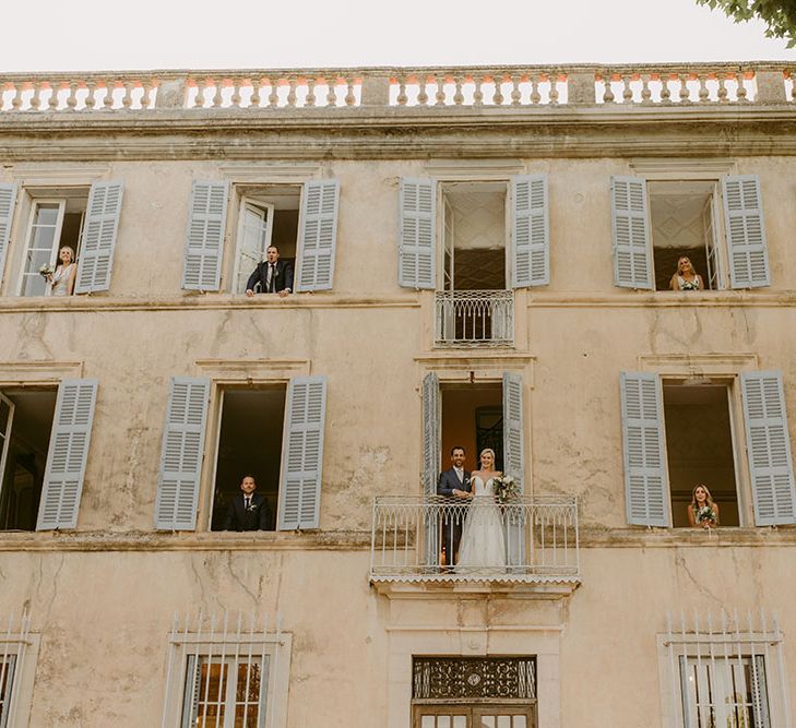 Bride & groom sit outside of open windows with their wedding party at the Chateau de Robernier