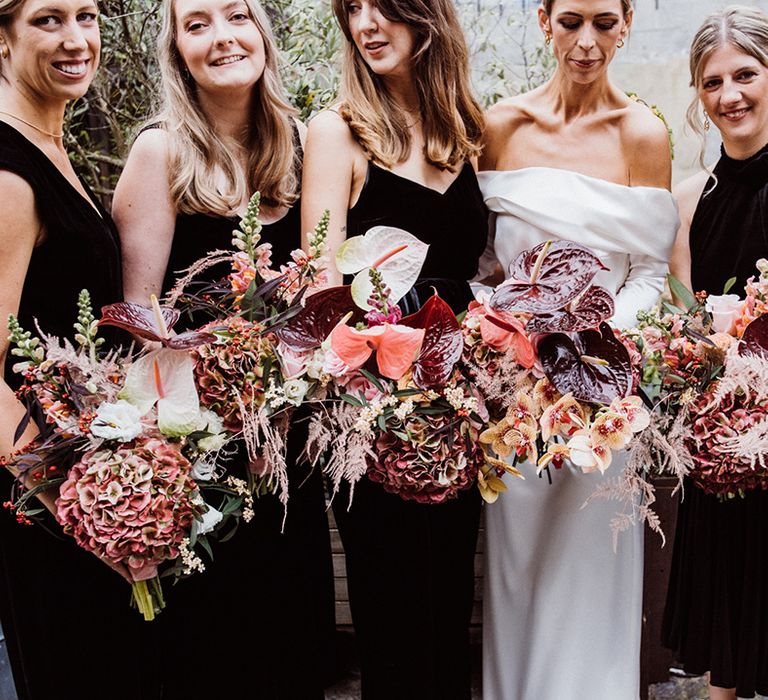 Bridal party with bridesmaids in black dresses and jumpsuits holding matching bouquets with anthuriums 