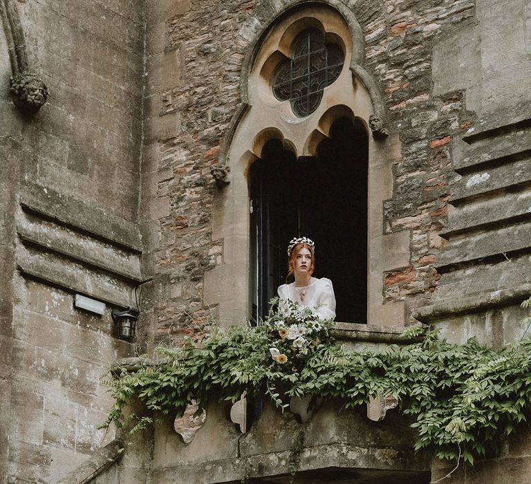 Bride in a gold crown looking over a veranda at Bishop's Palace Wells wedding venue in Somerset 