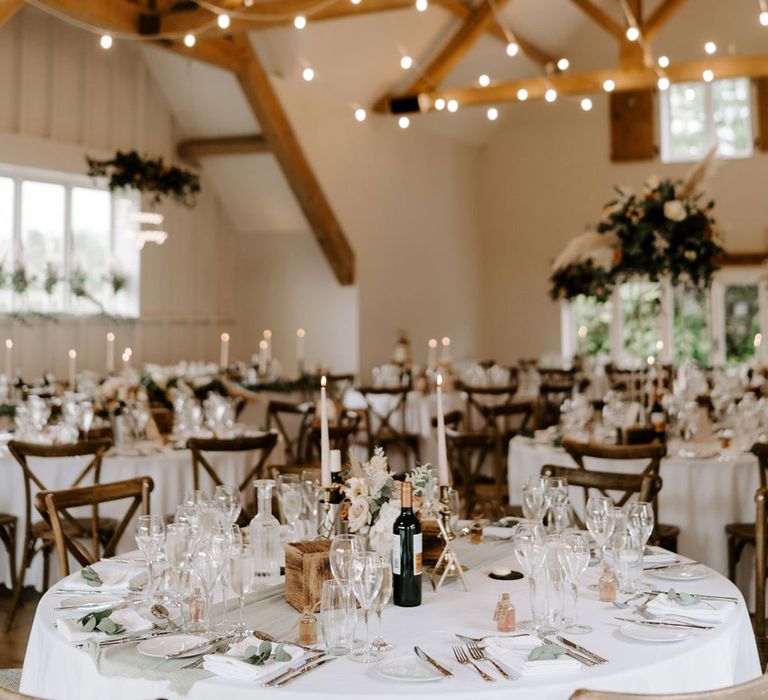 Sage green table runner and white tablecloths for round tables with white taper candles, pampas grass flower arrangements with fairy lights