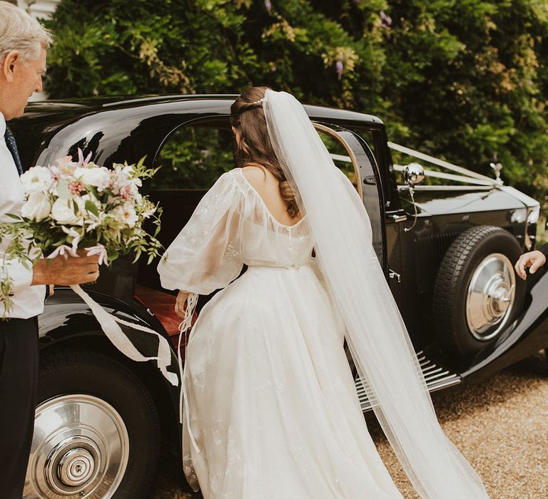 Bride in a Phillipa Lepley wedding dress and veil getting into her classic black vintage wedding car 