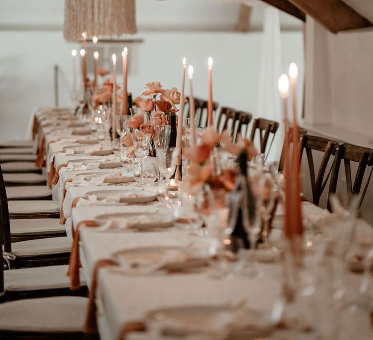 Soft pink and peach wedding tablescape with coloured flowers and taper candles and lots of white wedding drapery 