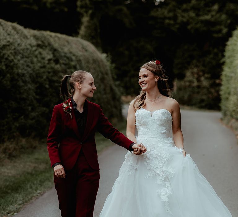 Cute couple portrait with bride in burgundy suit and red rose buttonhole with bride in a floral gown 