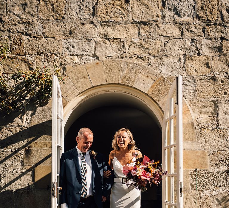 Bride wears satin slip wedding dress with belt and holds tropical bouquet 