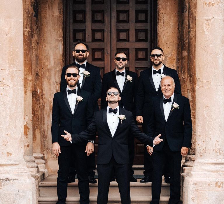 The groom and groomsmen in black tie wearing sunglasses