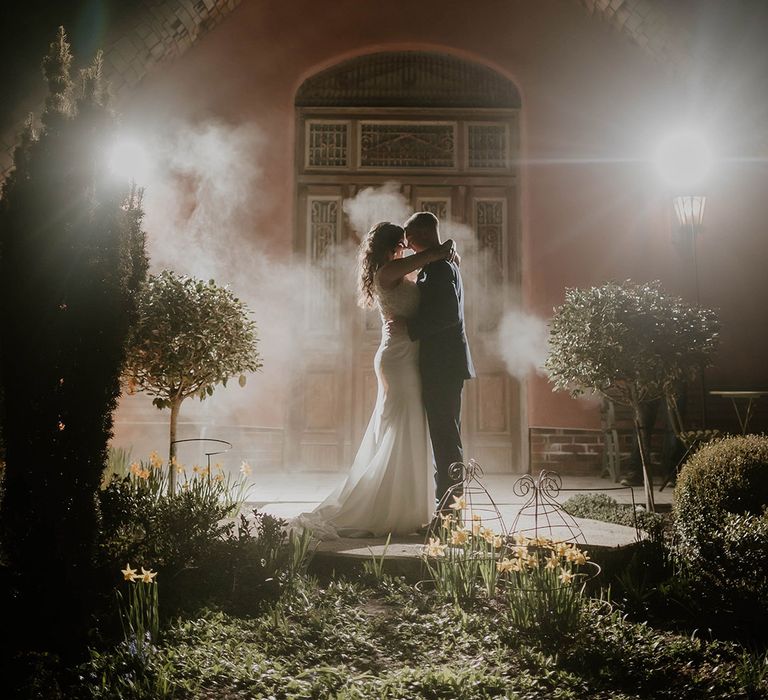 Bride & groom embrace outdoors at the Le Petit Chateau at night surrounded ambient smoke 