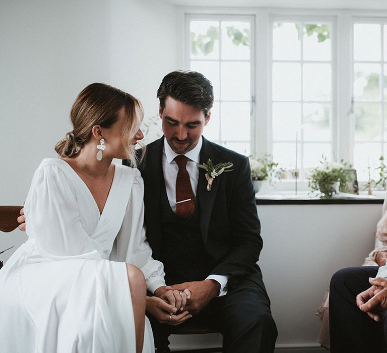 Bride wears silk wedding dress with wrap style whilst beside her groom wearing three piece suit 