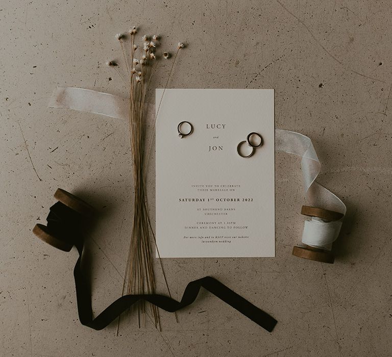 Minimal and chic black and white wedding invitation with wedding rings, dried flowers and ribbon 