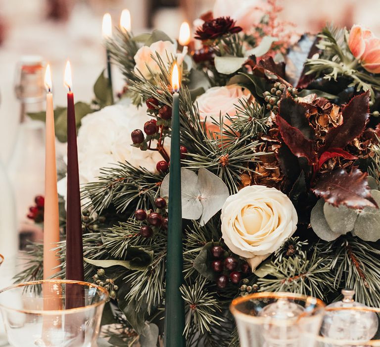 Orange, burgundy, green taper candles and winter flower arrangement with winter berries and red and white flowers 