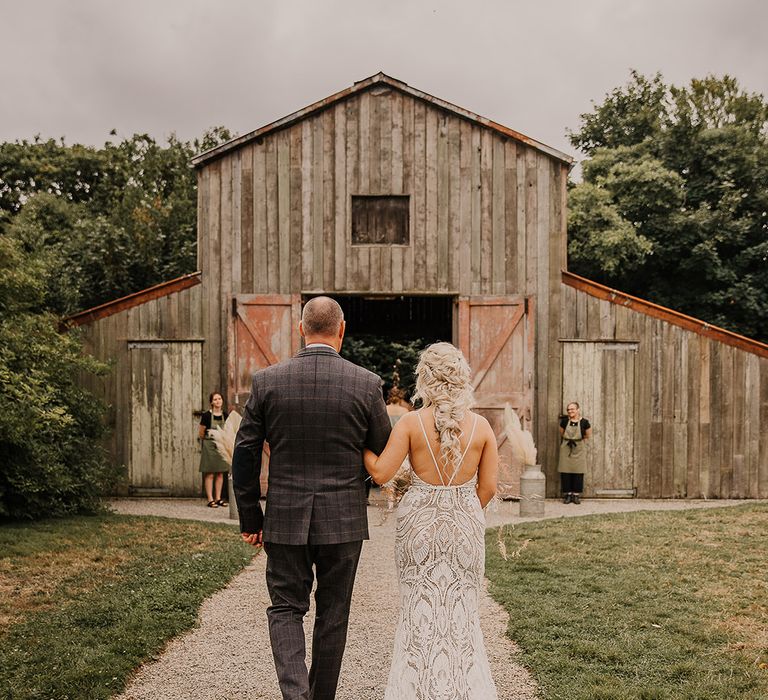 The father of the bride walks the bride into her rustic barn wedding  