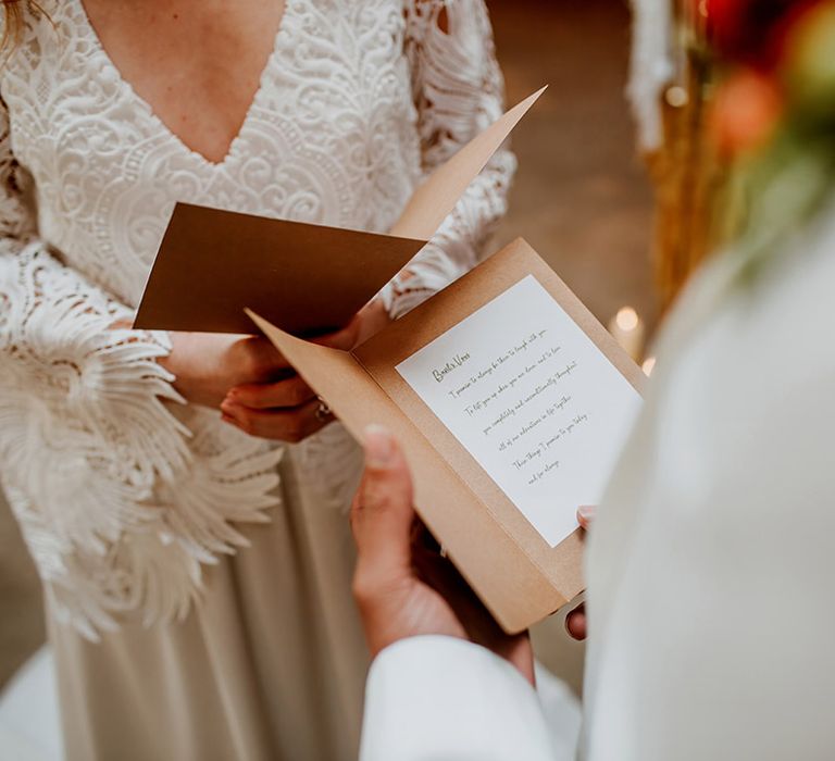 Bride and groom at boho winter-styled wedding in Kent barn venue reading each other their vows from rustic stationery 