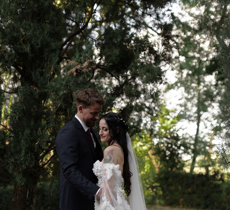 Bride wears floor-length veil whilst holding pampas grass bouquet and embracing her groom outdoors during destination wedding 