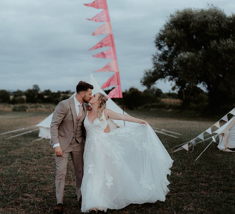 Bride & groom stand beside colourful bunting outdoors during festival wedding 