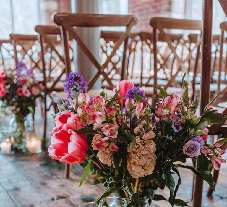 Alstroemeria, tulips, and roses make up this pink and purple flowers arrangement in a glass vase with candles in glass jars and leaf decor 