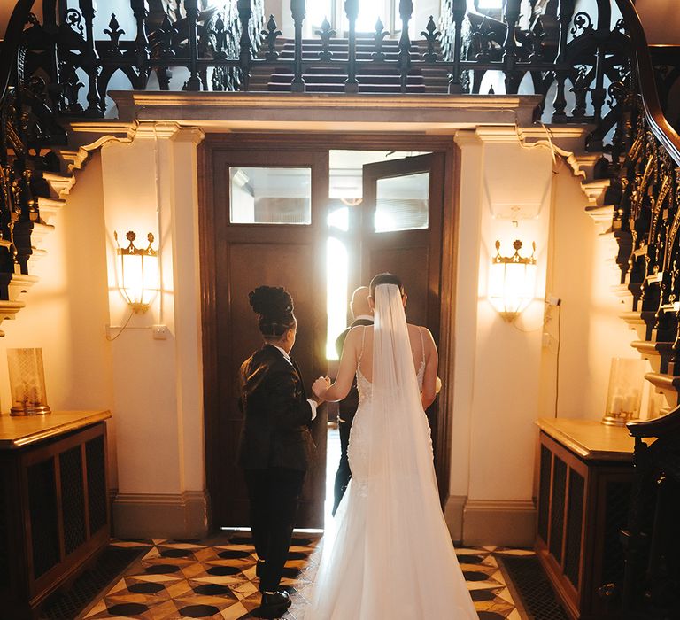 Bride in lace sleeveless v neck Enzoani wedding dress with tulle finish and church length embroidered lace 3d appliqué veil holding hands with bride in black-tie tuxedo at Grittleton House