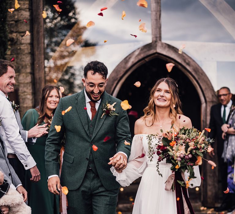 Yellow and orange rose petal confetti moment for autumnal November wedding as the bride and groom exit from the ceremony