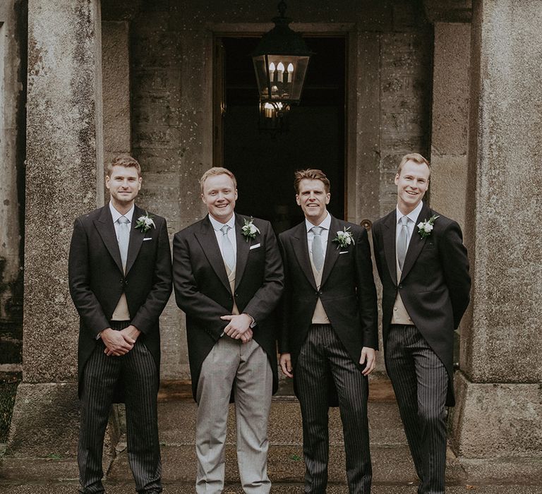 Groomsmen stand together in morning suits with sage green ties and different style trousers 