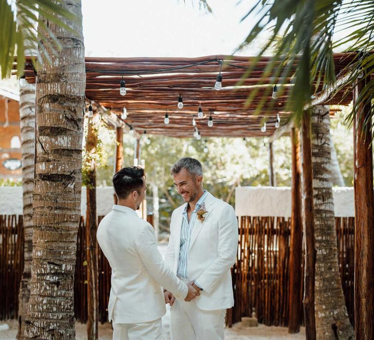 Grooms in complimenting white double breasted wedding suits on Holbox beach at destination LGBTQ+ wedding 