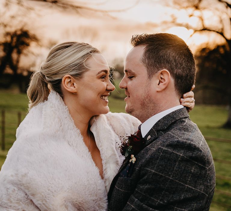 Bride in faux fur shawl for chilly spring wedding evening with the groom in grey suit 