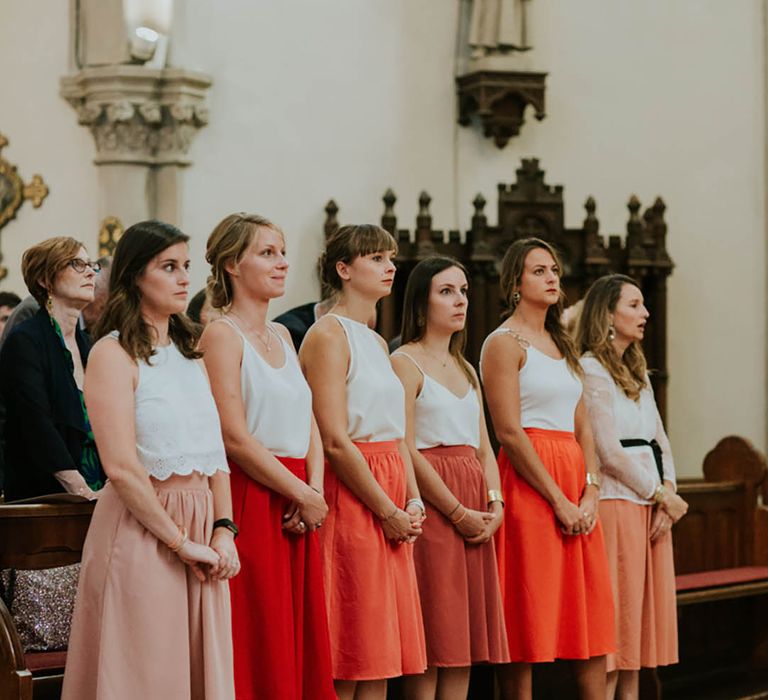 Bridesmaids in two piece sets with white tops and different shades of orange midi skirts 