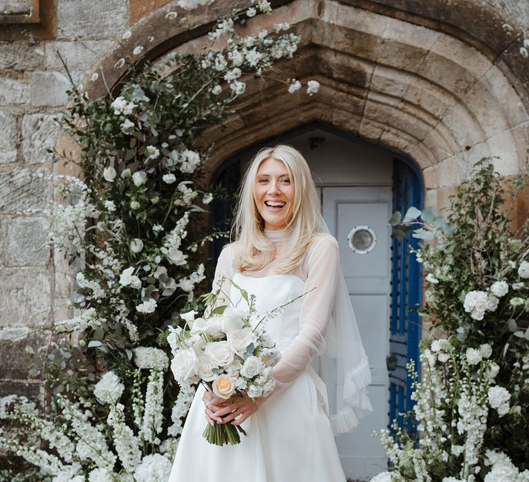 Bride in strapless wedding dress with mesh overlay top wearing ruffle veil carrying white bouquet 