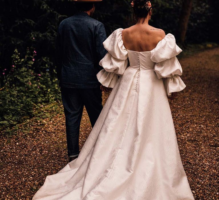 Bride in layered puff sleeve Jesus Peiro wedding dress walking hand in hand with the groom 