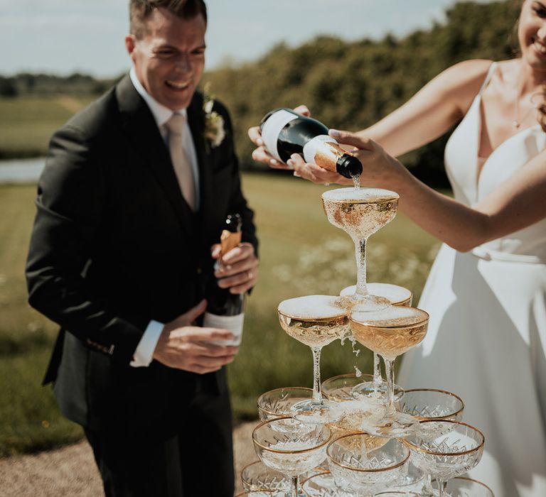 Bride pours champagne over champagne tower with gold rimmed coupe glasses 