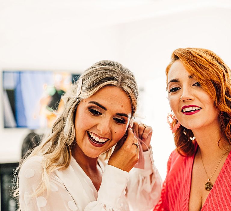 bride in a long sleeve jumpsuit putting on earrings on the wedding morning 