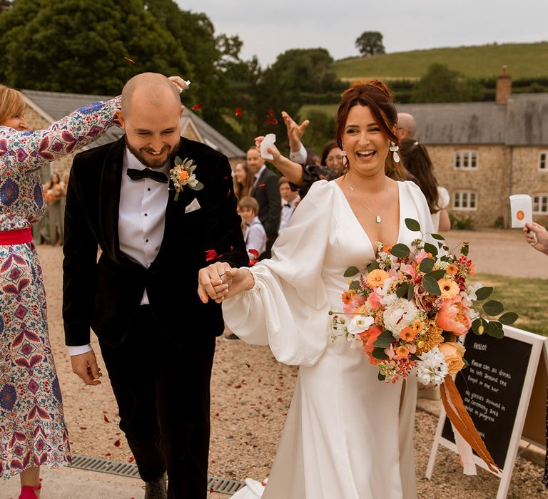 Groom in black tuxedo with bride in a satin balloon sleeve Watters wedding dress at their retro 70s wedding 