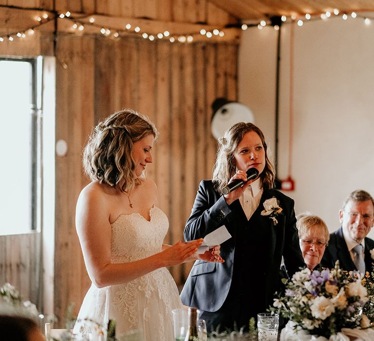 bride in a lace wedding dress and bride in a navy suit perform a joint wedding speech at Stanford Farm wedding 