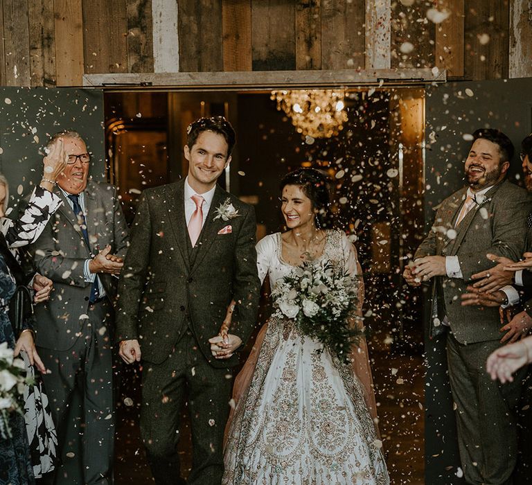 The bride and groom walk out of the ceremony together as the guests throw confetti 