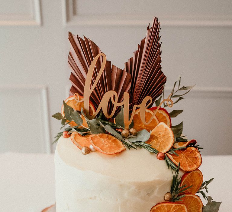 Single tier white iced wedding cake with dried orange slices and palm leaves with love cake topper 